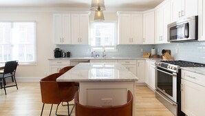 A modern kitchen with white cabinets, a central island, stainless steel appliances, and a pendant light. - Stay just a 3-minute walk from the beach in this stunning luxury home located between Ocean Grove & Asbury Park. Perfect for large families and groups, this spacious retreat offers modern amenities, multiple outdoor spaces, and everything you need. (Ocean Grove)