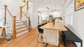 A modern kitchen with white cabinets, a wooden dining table, and a black bench.