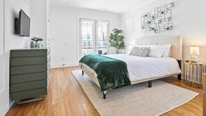 A modern bedroom with a bed, a dresser, a TV, and a plant.
