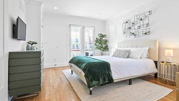 Une chambre à coucher moderne avec un lit, une commode, un téléviseur et une plante.