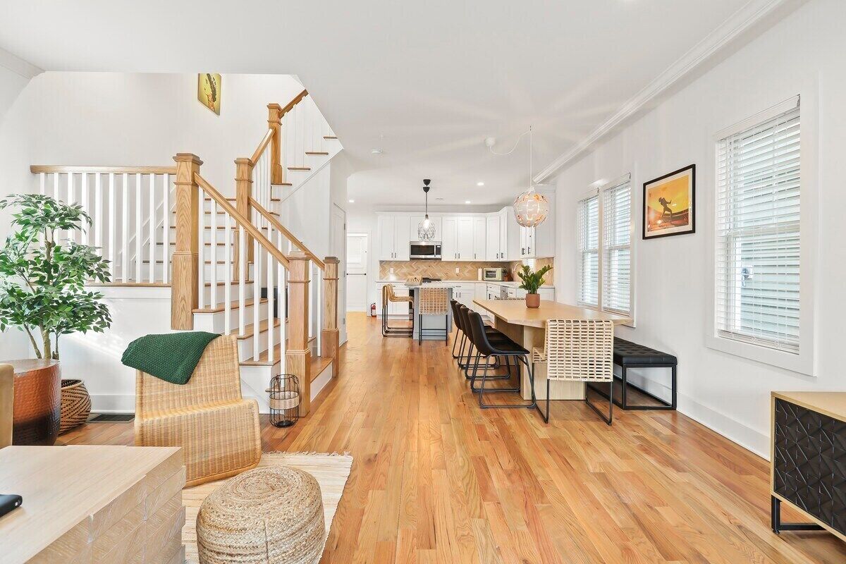 Un vaste espace de vie agrémenté d’un escalier en bois, une cuisine avec des meubles blancs et un coin repas doté d’une longue table.