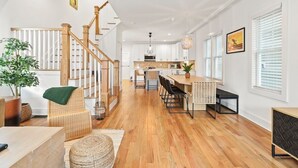 A spacious living area with a wooden staircase, a kitchen with white cabinets, and a dining area with a long table.