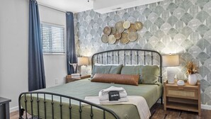 A bedroom with a bed, bedside tables, a wall with decorative patterns, and a window with curtains.