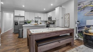 A modern kitchen with white cabinets, stainless steel appliances, and a central island with a pool table.