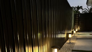A modern outdoor pathway with a metal fence and gravel, illuminated by ground lights.