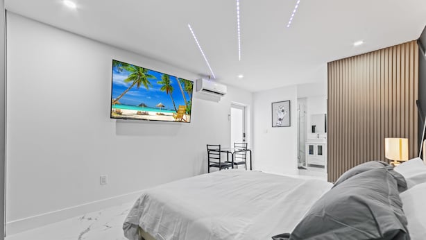 A modern bedroom with a large bed, a TV mounted on the wall, and a wooden panel on the wall.