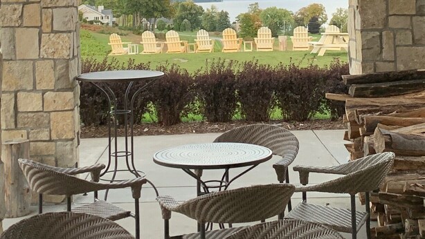 A stone archway overlooking a patio area with wicker furniture and a view of a lake and distant buildings. - NEW Modern Condo, King Beds, Rooftop Hot Tubs, Near Downtown, Quiet! (Traverse City)