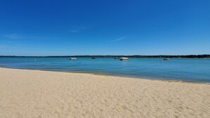 A sandy beach with calm water and several boats anchored in the distance. - NEW Modern Condo, King Beds, Rooftop Hot Tubs, Near Downtown, Quiet! (Traverse City)