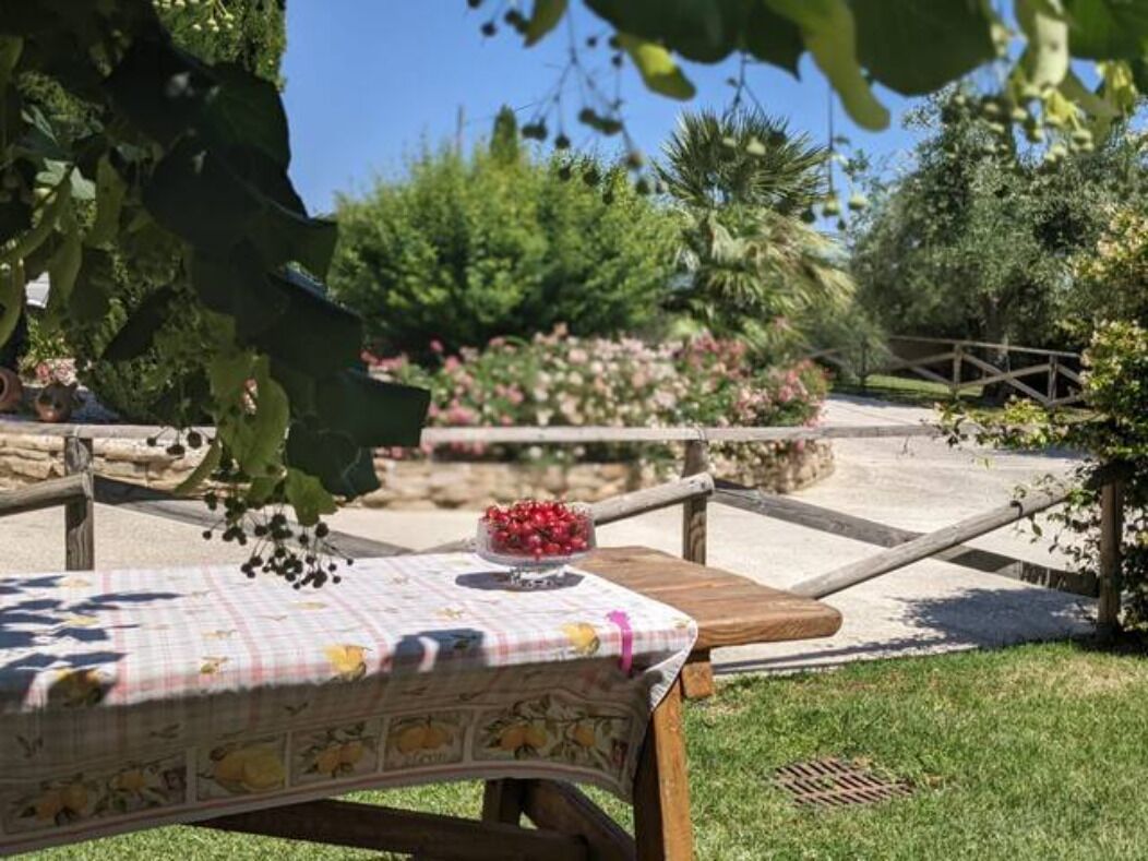 A picnic table with a floral tablecloth and a bowl of fruit in a garden setting.