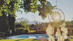 A dreamcatcher hanging over a swimming pool with a lush green lawn and trees in the background. - Casa Kikenda Relaise, an enchanted garden for your dream vacation. (Treia)