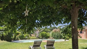A backyard with two lawn chairs under a tree, a swimming pool, and a building in the background. - Casa Kikenda Relaise, an enchanted garden for your dream vacation. (Treia)