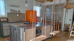 A modern kitchen with a central island, wooden flooring, and a hanging swing chair. - Casa Kikenda Relaise, an enchanted garden for your dream vacation. (Treia)