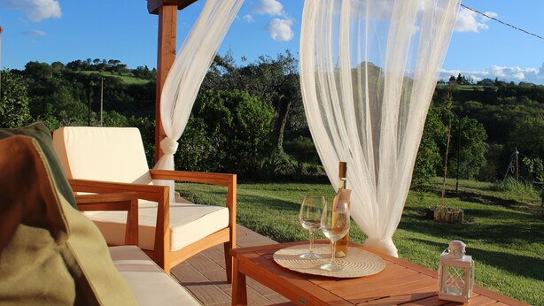 A wooden table with a bottle and two glasses, set on a patio with a view of a green landscape. - Casa Kikenda Relaise, an enchanted garden for your dream vacation. (Treia)