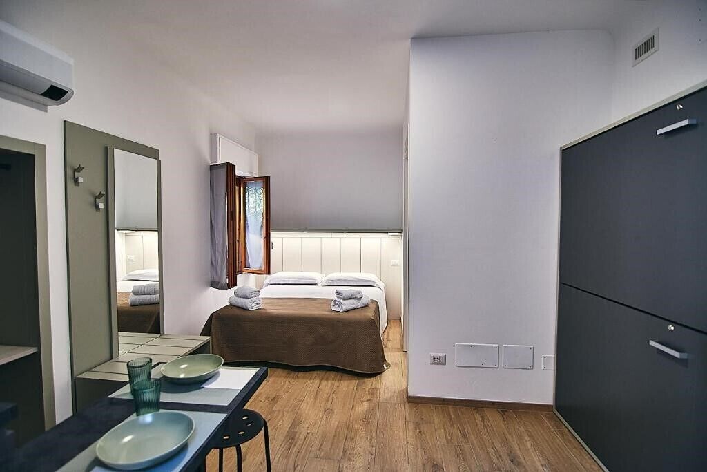 Camera d'albergo compatta con un letto, un comodino con specchio, un armadio e una piccola area salotto.