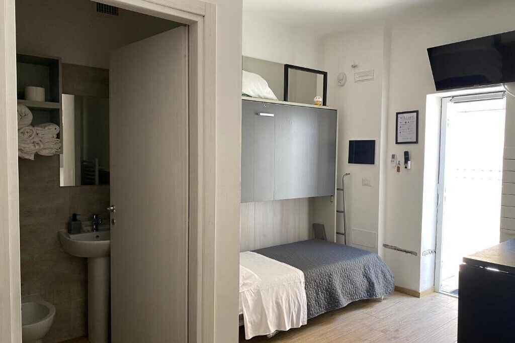 Een kleine slaapkamer met een stapelbed, een nachtkastje, een klein raam, en een badkamer met een wastafel en toilet.