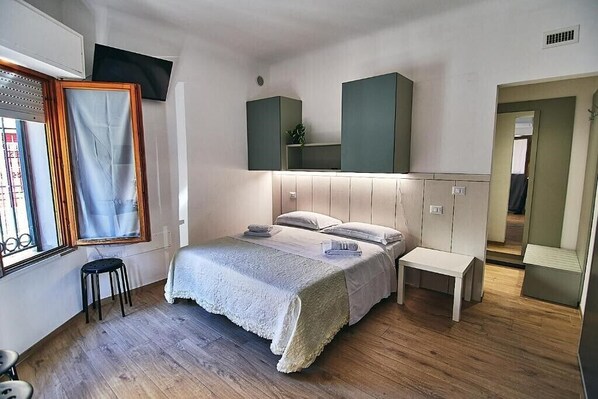 A bedroom with a bed, a small stool, a bench, a TV mounted on the wall, and a mirror.