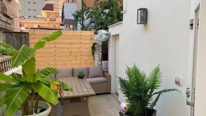 A small patio with a wooden table and a sofa, surrounded by potted plants.