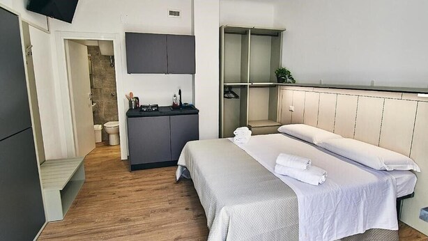 A modern hotel room with a bed, a small kitchenette, a TV, and a walk-in closet.