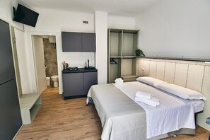 A modern hotel room with a bed, a small kitchenette, a TV, and a walk-in closet.