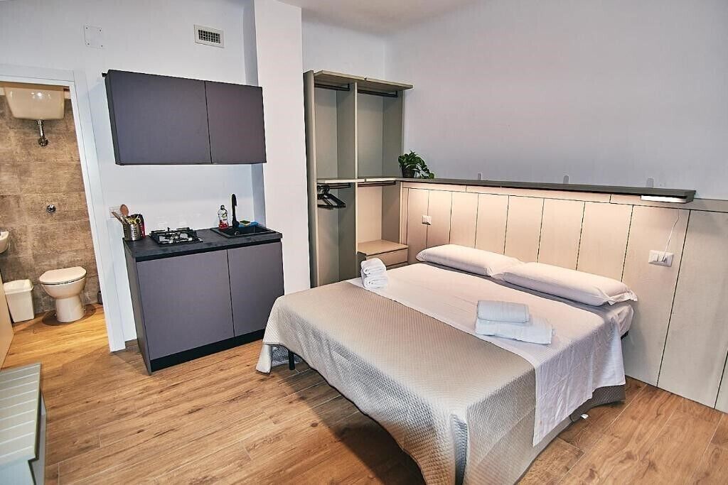 A modern bedroom with a bed, bedside tables, a built-in wardrobe, and a small kitchenette.