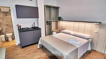 A modern bedroom with a bed, bedside tables, a built-in wardrobe, and a small kitchenette.