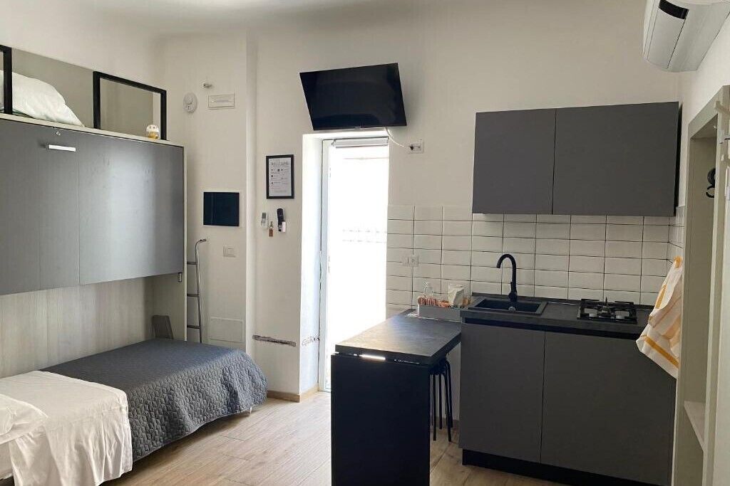 A compact room with a bunk bed, a small kitchenette, and a flat-screen TV mounted above the bed.