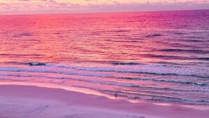 Una playa con olas y una persona de pie sobre la arena.