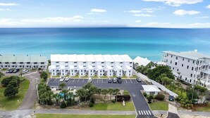 Un hotel frente a la playa con varios edificios blancos, un estacionamiento y una zona de piscina.