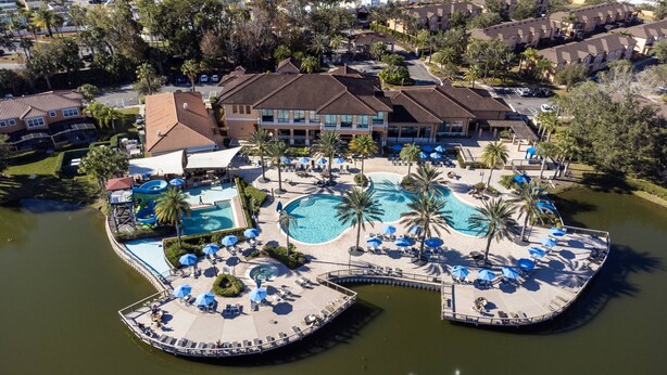 An aerial view of a resort with multiple swimming pools, palm trees, and a dock with lounge chairs. - 3BR house with hot tub in Regal Oaks Resort (Kissimmee)