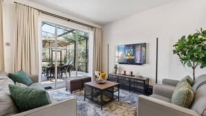 A modern living room with a sofa, a coffee table, and a TV mounted on the wall. - 3BR house with hot tub in Regal Oaks Resort (Kissimmee)