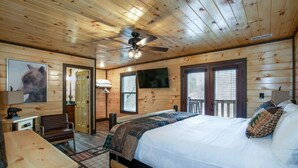 Une chambre confortable, aménagée dans le style d’un chalet, avec un plafond en bois, un lit recouvert d’une courtepointe, un bureau avec une chaise et une fenêtre équipée de stores.