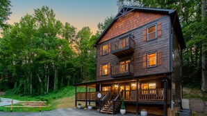 Une cabane en rondins à deux étages, dotée d’un balcon, d’une véranda et d’une allée menant à un banc.
