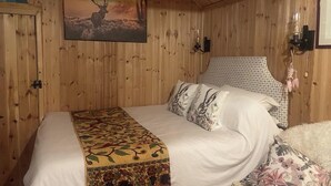 A wooden-paneled room with a bed, a painting of a deer, and a patterned headboard. - 1 Bedroom Cabin Sleeps 2, Private Garden, Wifi (Camelford)