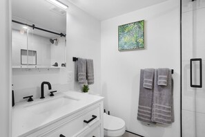 Un baño moderno con un lavamanos blanco, grifo negro y un espejo grande. Hay dos toallas colgadas en ganchos y una planta verde sobre el mostrador.