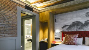 A hotel room with a brick wall, a wooden headboard, a bed with white bedding, a red telephone, and a painting of trees on the wall. - Hotel La Pau  (Barcelona)