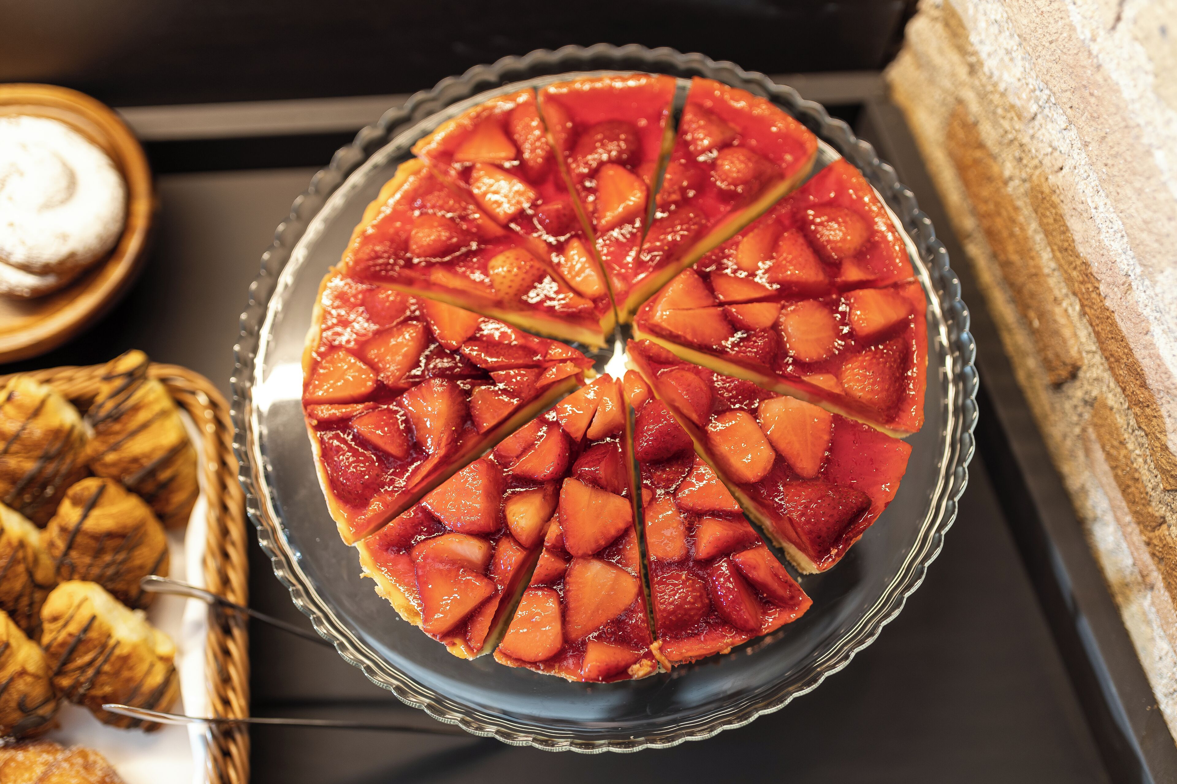 Una tarta de frutas redonda sobre un plato de vidrio, acompañada de pasteles y un pastel.