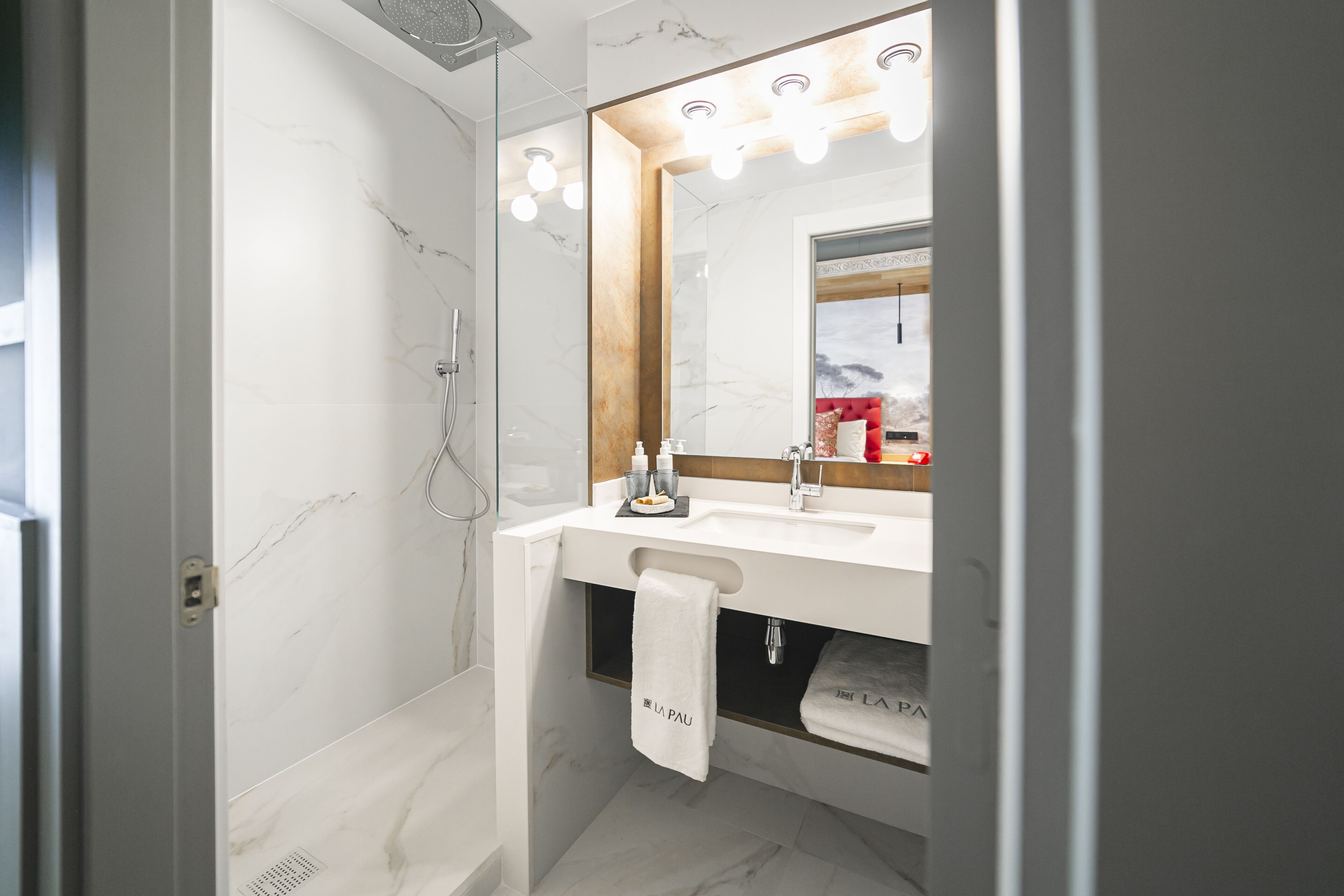 A modern bathroom with a marble shower, a white sink, and a large mirror with lights.