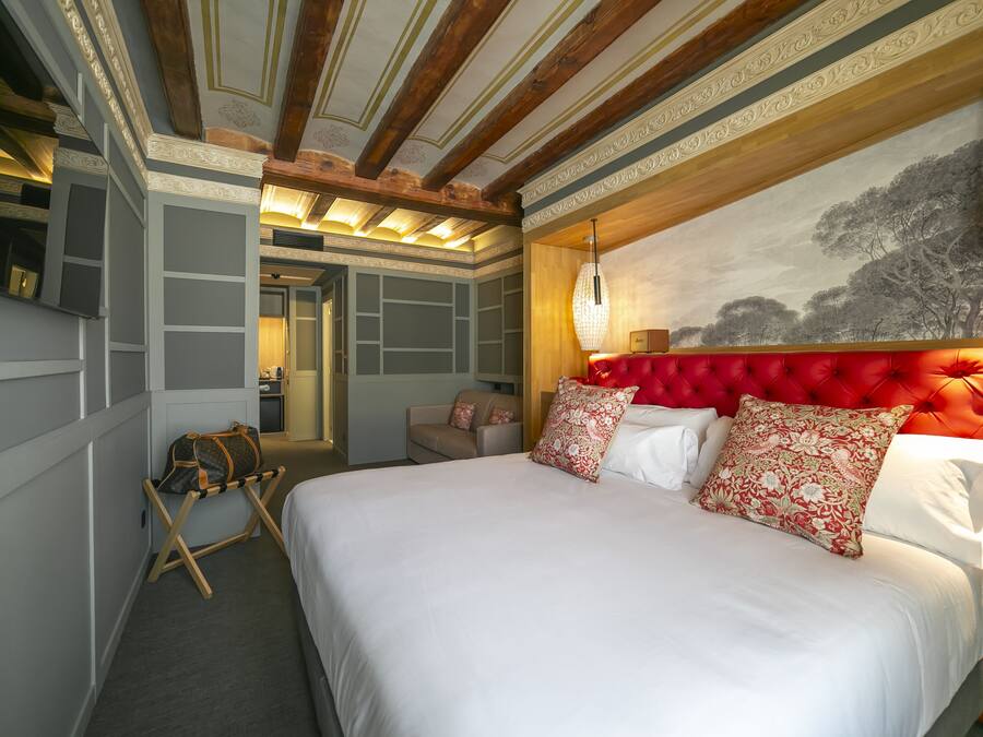 Un dormitorio con una cama grande, un cabecero tapizado rojo y una lámpara de pared.