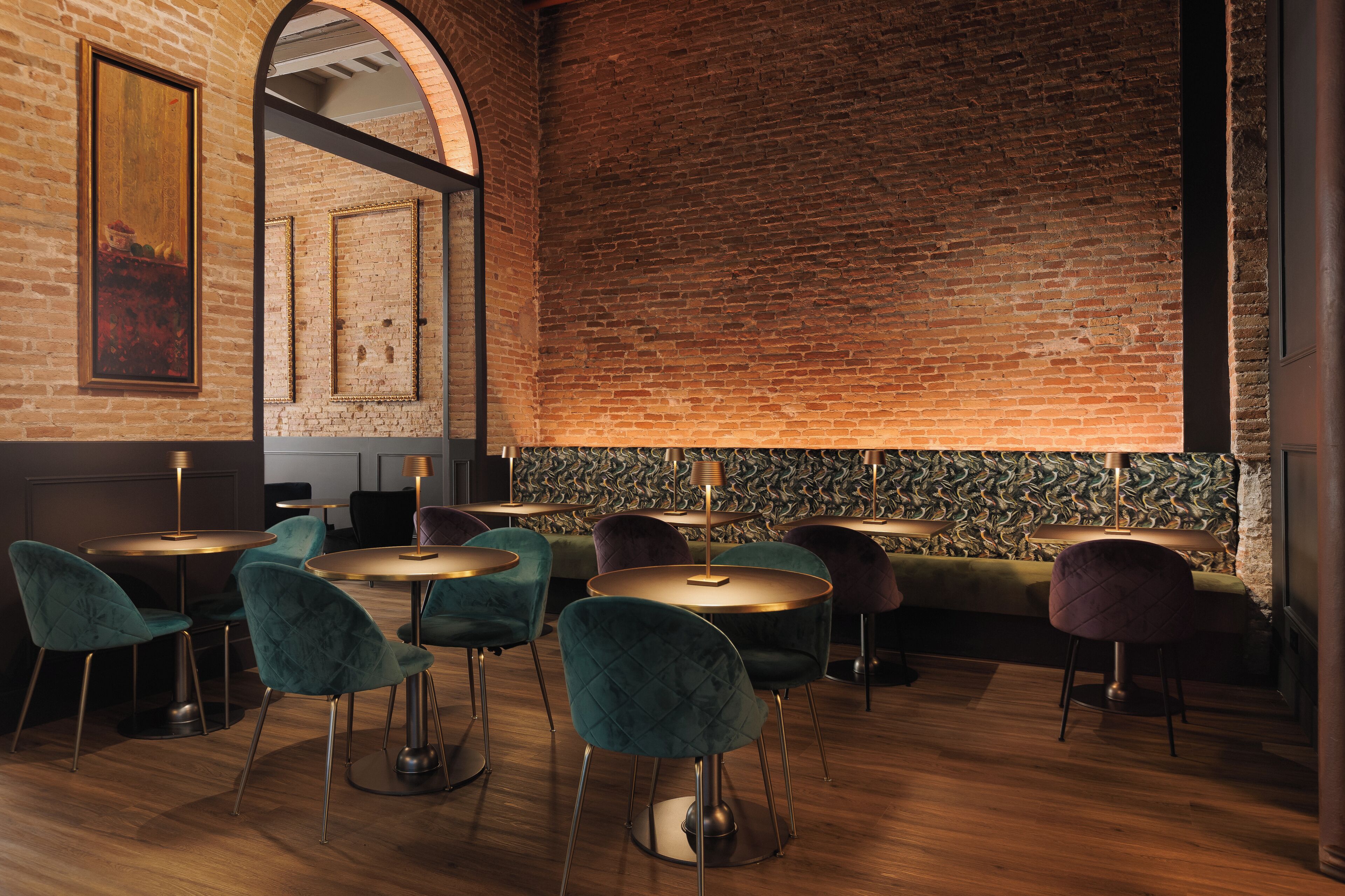 A restaurant with brick walls, round tables, and teal chairs.