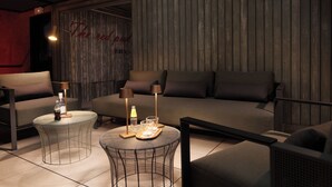 A cozy lounge area with a sofa, two round tables with lamps, and a wooden wall with a sign. - Hotel La Pau  (Barcelona)
