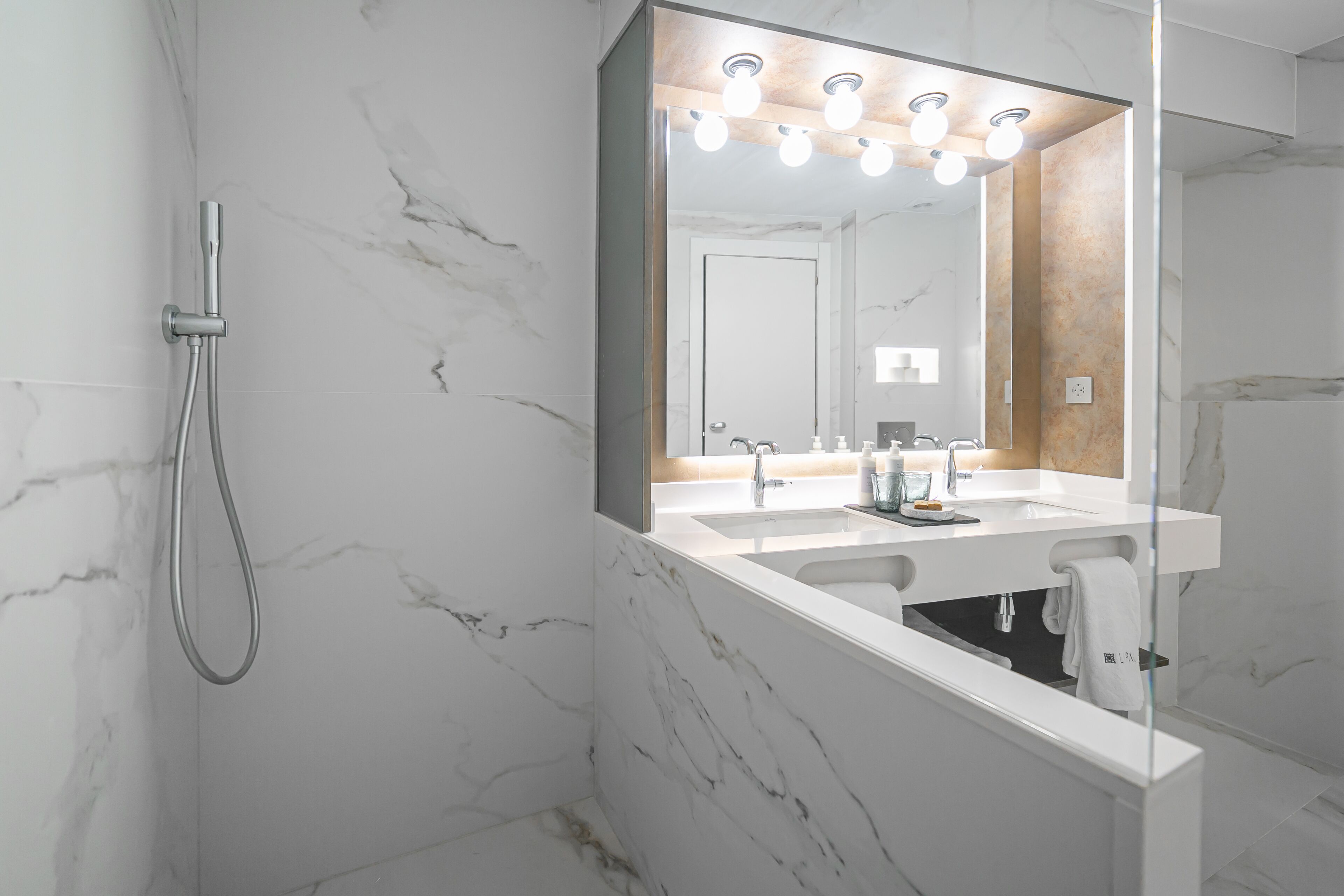 A modern bathroom with a marble wall, a shower, and a vanity with a mirror.