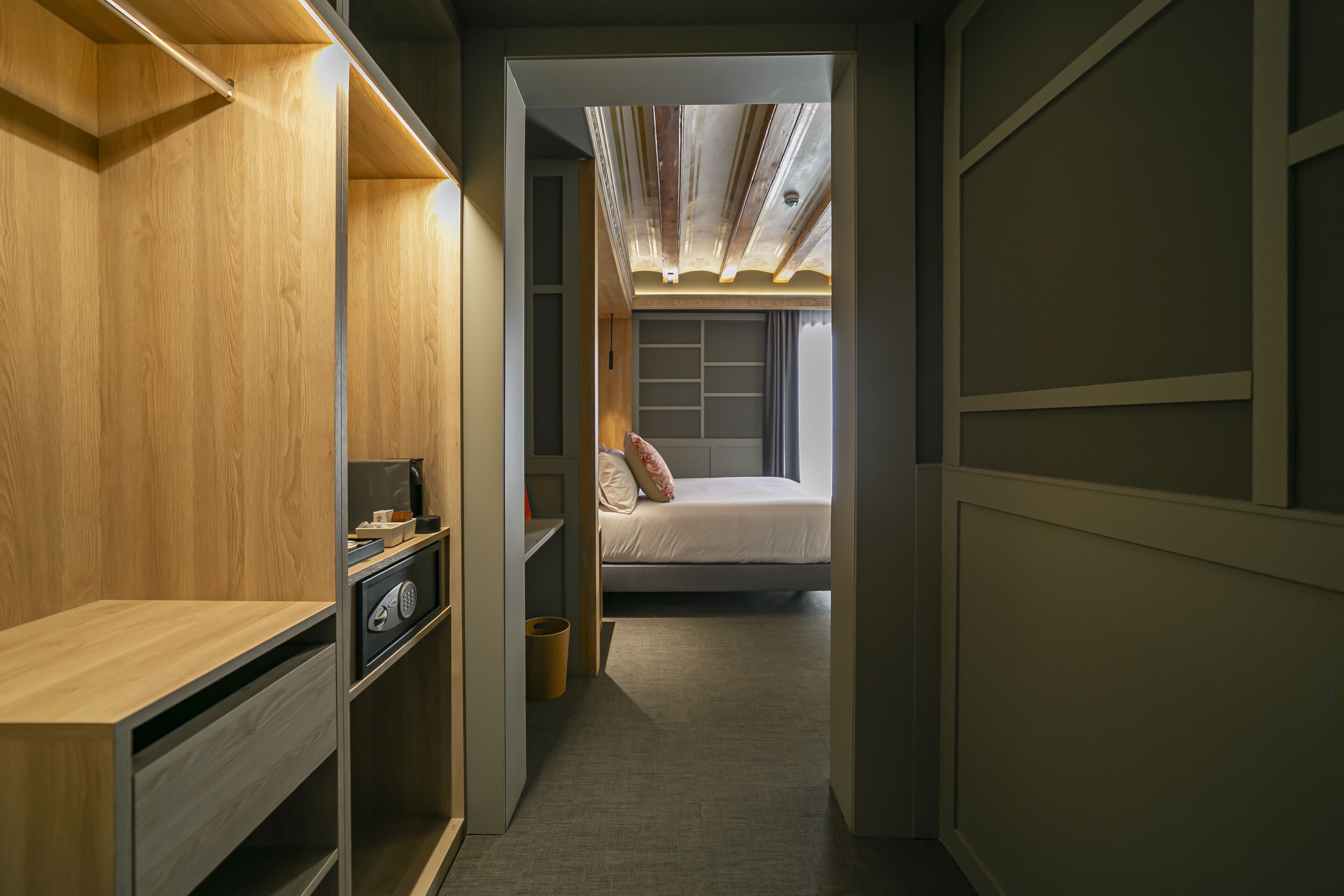 A narrow hallway leading to a bedroom with a bed, a desk, and a wardrobe.