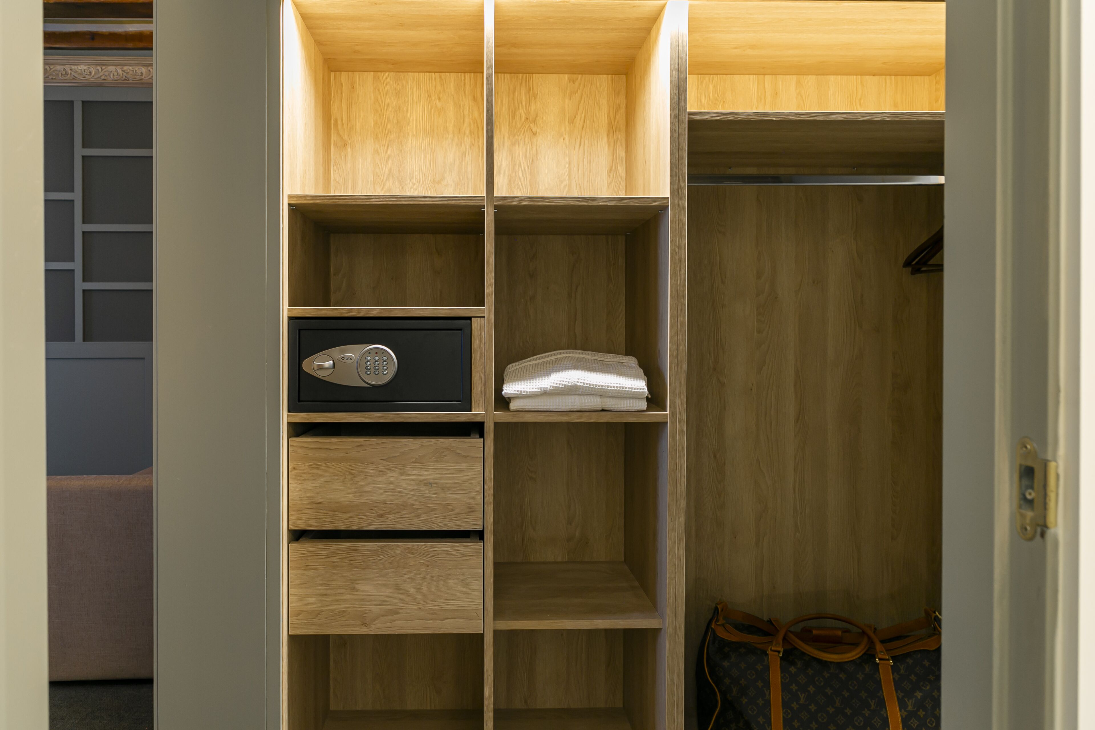 A wooden closet with shelves, a safe, and a handbag.