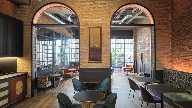 A modern interior with brick walls, arched windows, and a mix of round and rectangular tables and chairs. - Hotel La Pau  (Barcelona)