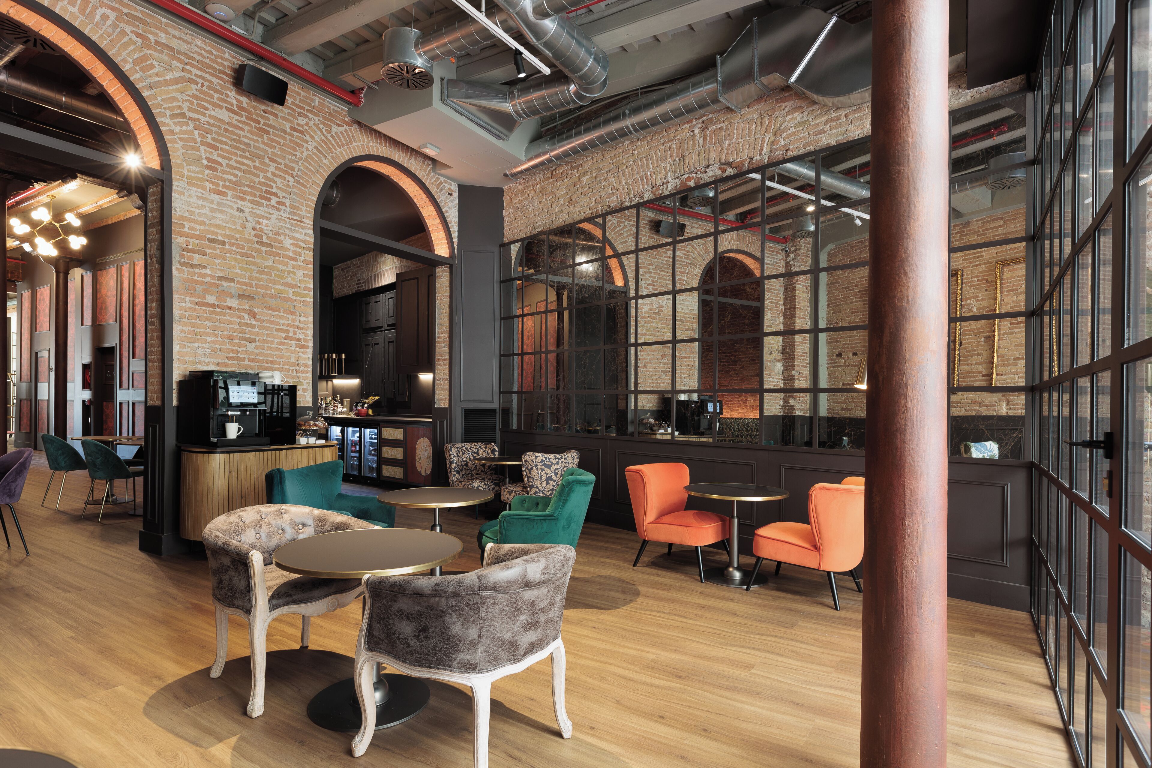 Un intérieur moderne avec des murs en briques, de grandes fenêtres et un agencement varié des espaces de détente, comprenant des tables et des chaises rondes.