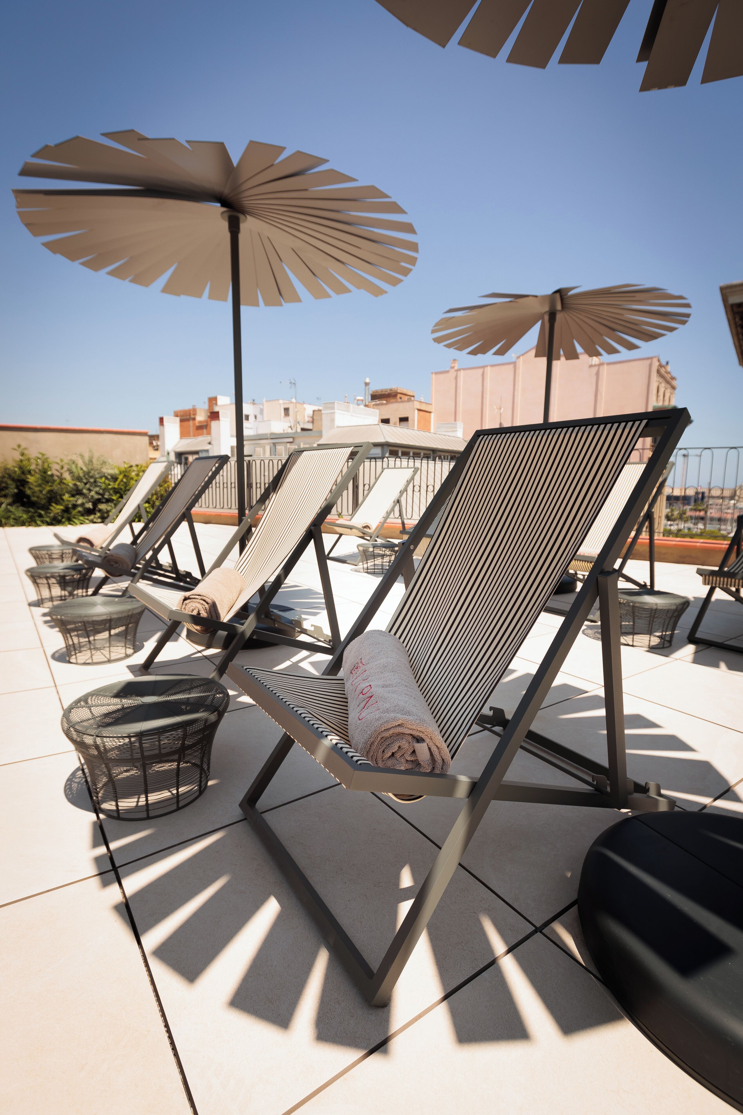 Un área de estar en la azotea con sillones solárium, sombrillas y vistas despejadas del horizonte de la ciudad.