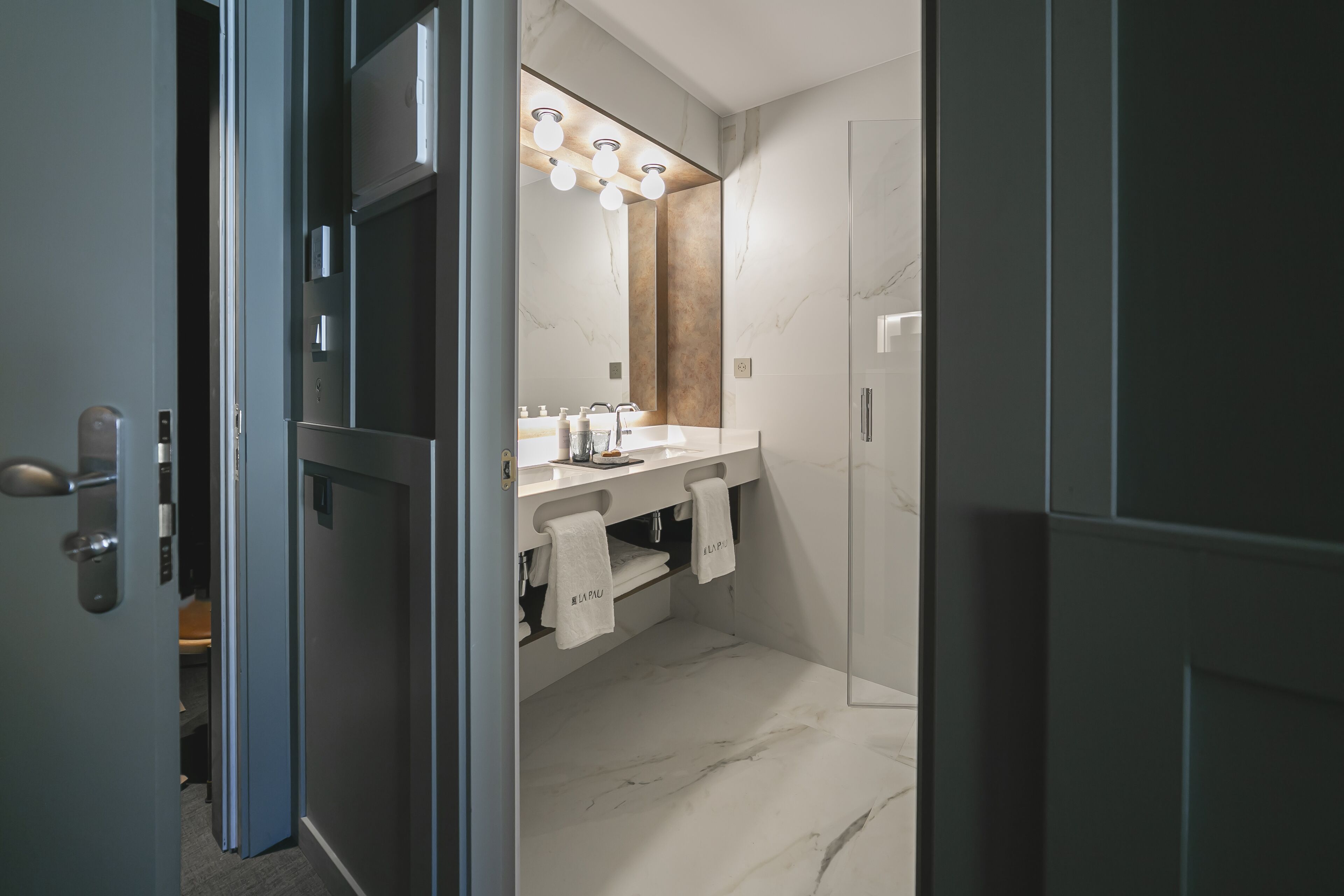 Un baño moderno con piso de mármol, un espejo grande y una tocador con lavamanos y barra para toallas.