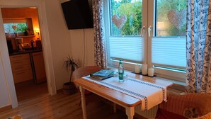 A dining area with a table, chairs, a television, and a window with curtains.