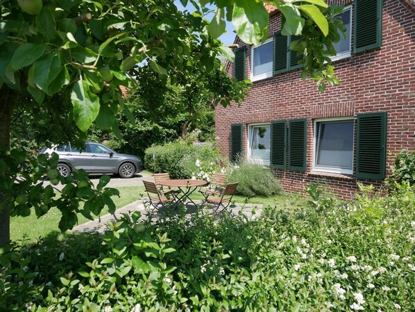 A brick house with a car parked in the driveway, a wooden bench, and a garden with various plants.