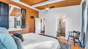 Une chambre avec un grand lit, un ventilateur de plafond et un mur en briques.